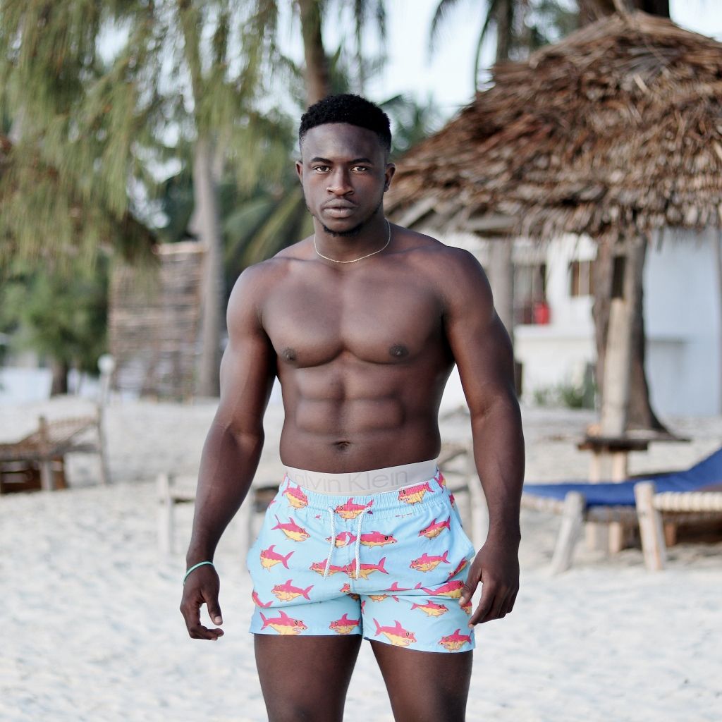 Beach portrait of a man in patterned swim shorts under palm trees