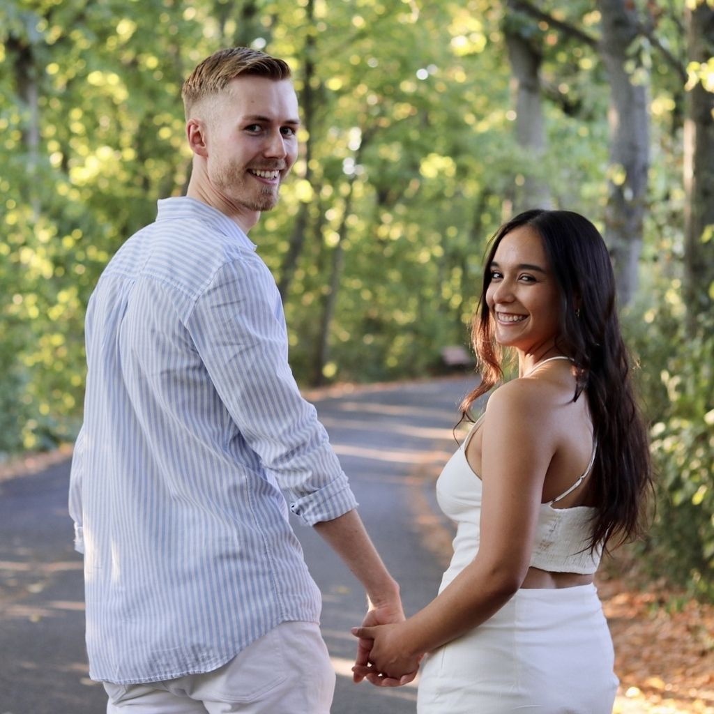 Couple holding hands and looking back on a sunlit forest path