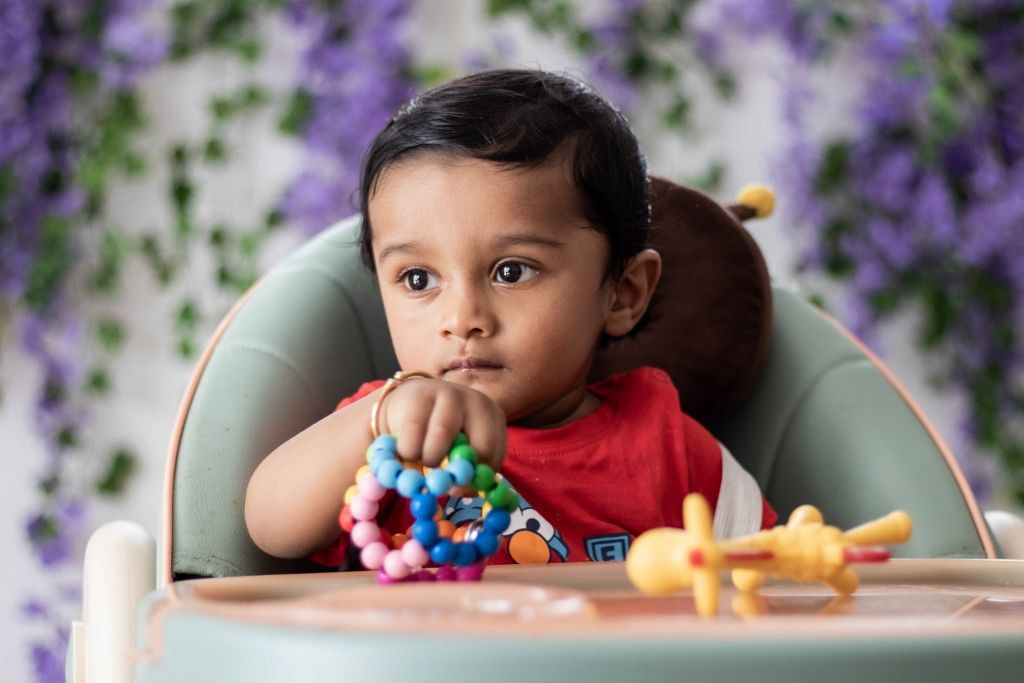 Indoor portrait of a baby in a high chair against a purple floral backdrop