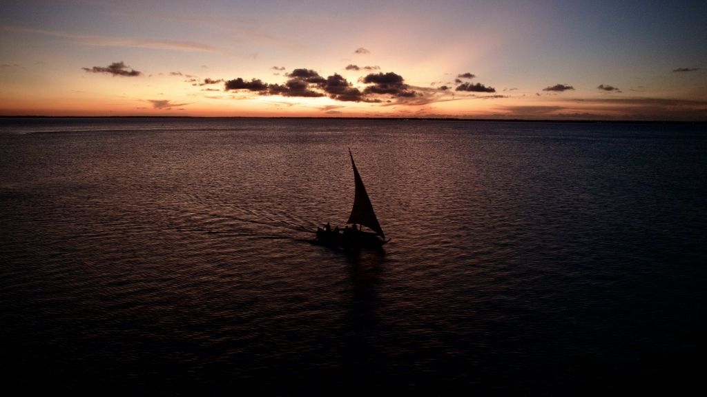 Silhouetted dhow sailing boat against a coastal sunset